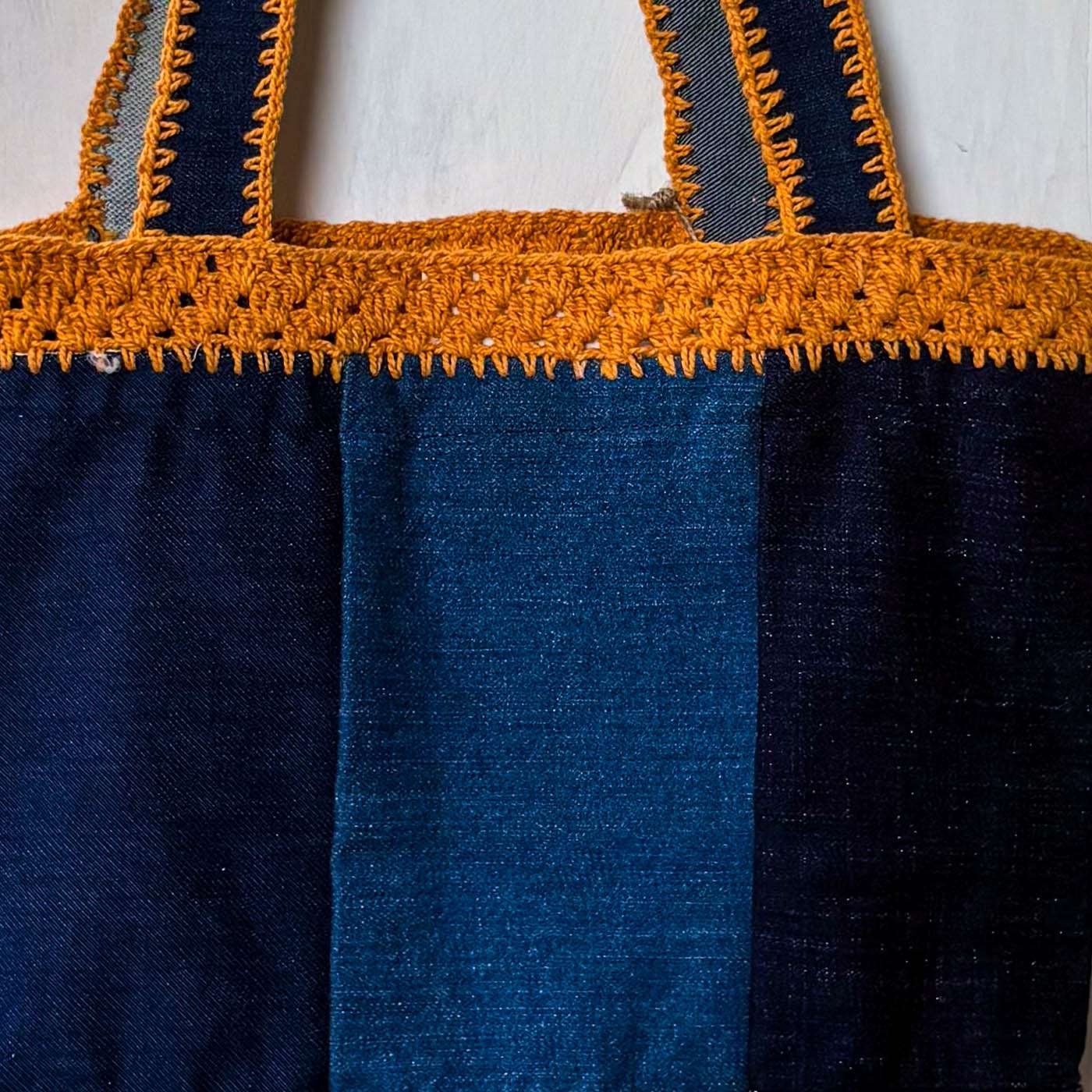 Blue tote bag with orange crochet top handle on a white background