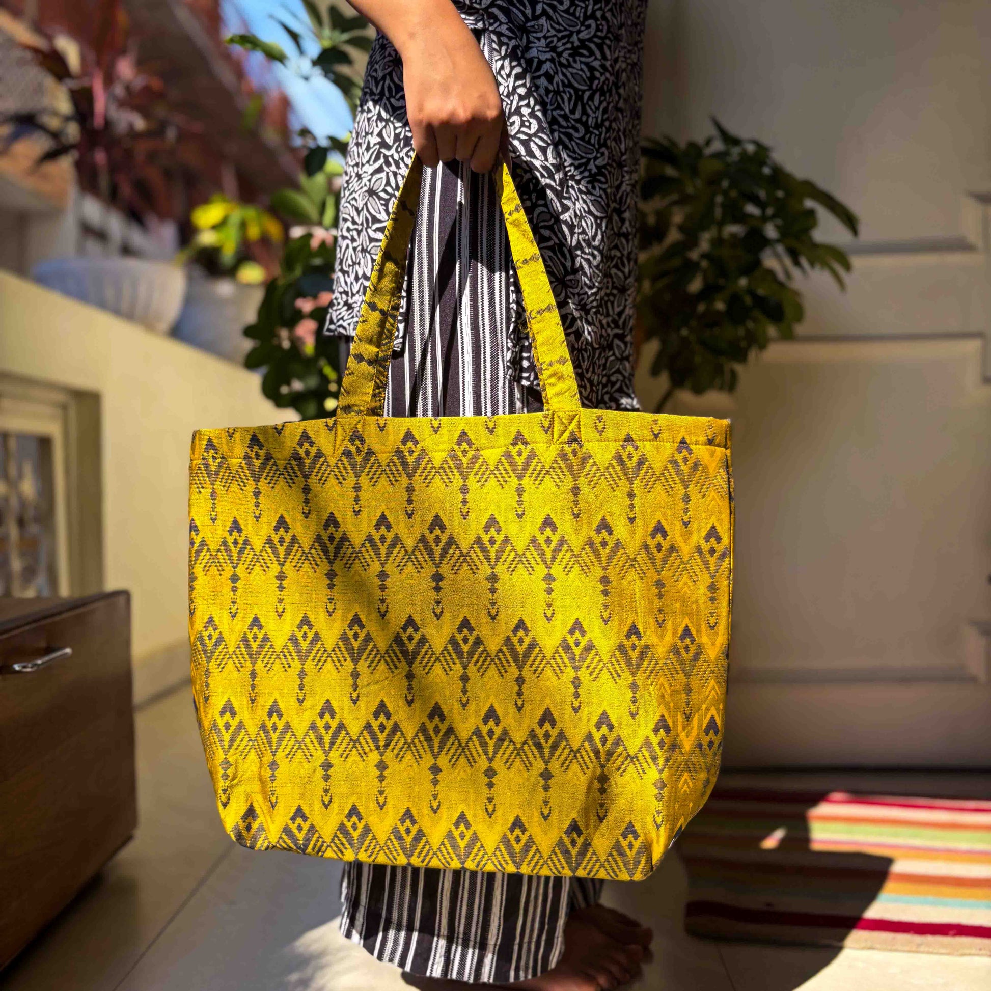Person holding a yellow tote bag with a ikat pattern in an indoor setting.