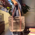 Person holding a Bronze tote bag with decorative straps in an indoor setting.