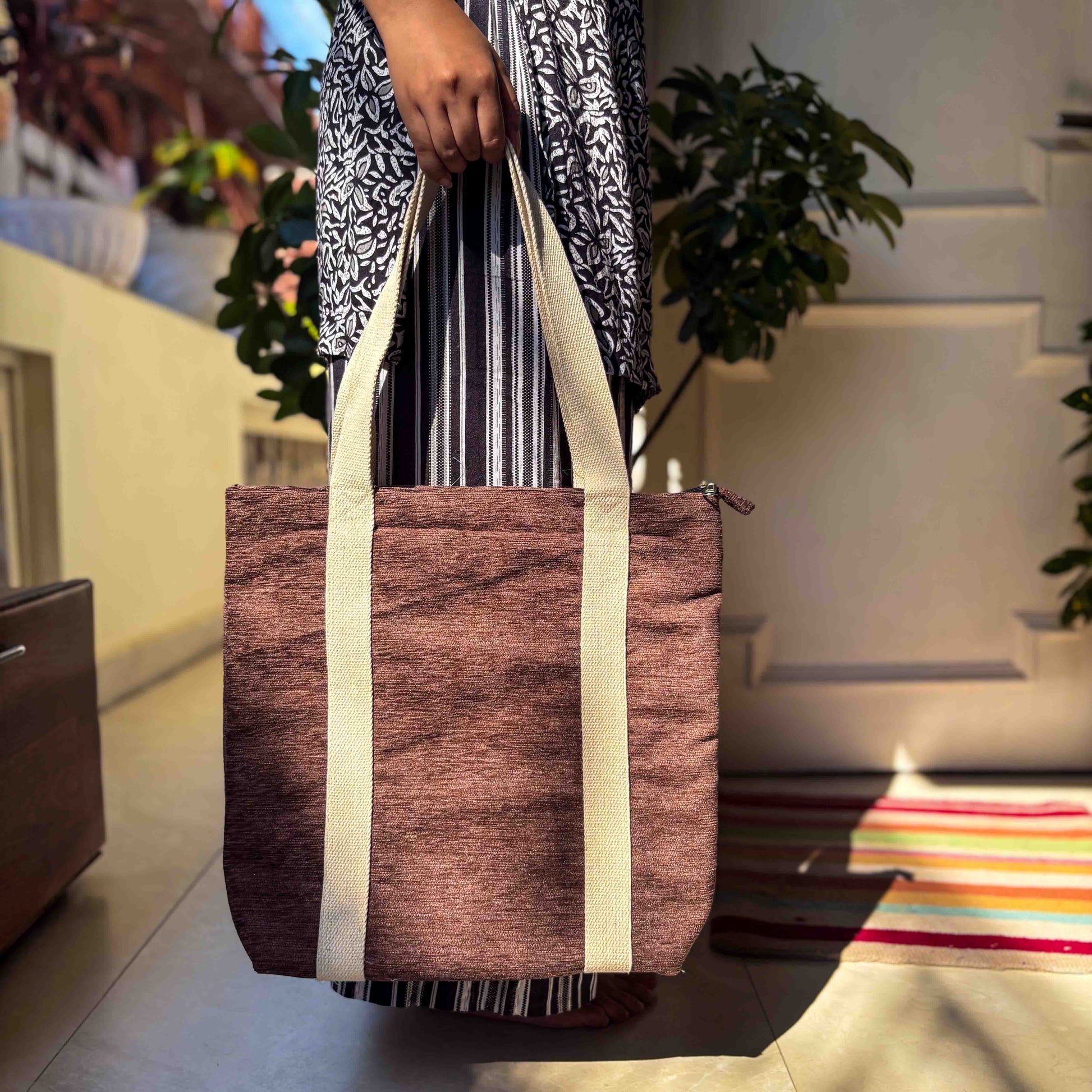 Person holding a brown tote bag with white straps in an outdoor setting