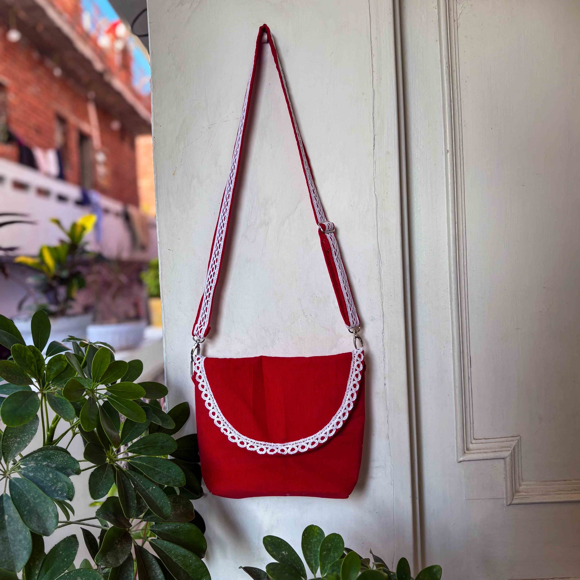 Red handbag with white lace details hanging on a white door