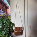 Brown leather handbag with white macramé strap hanging on a door