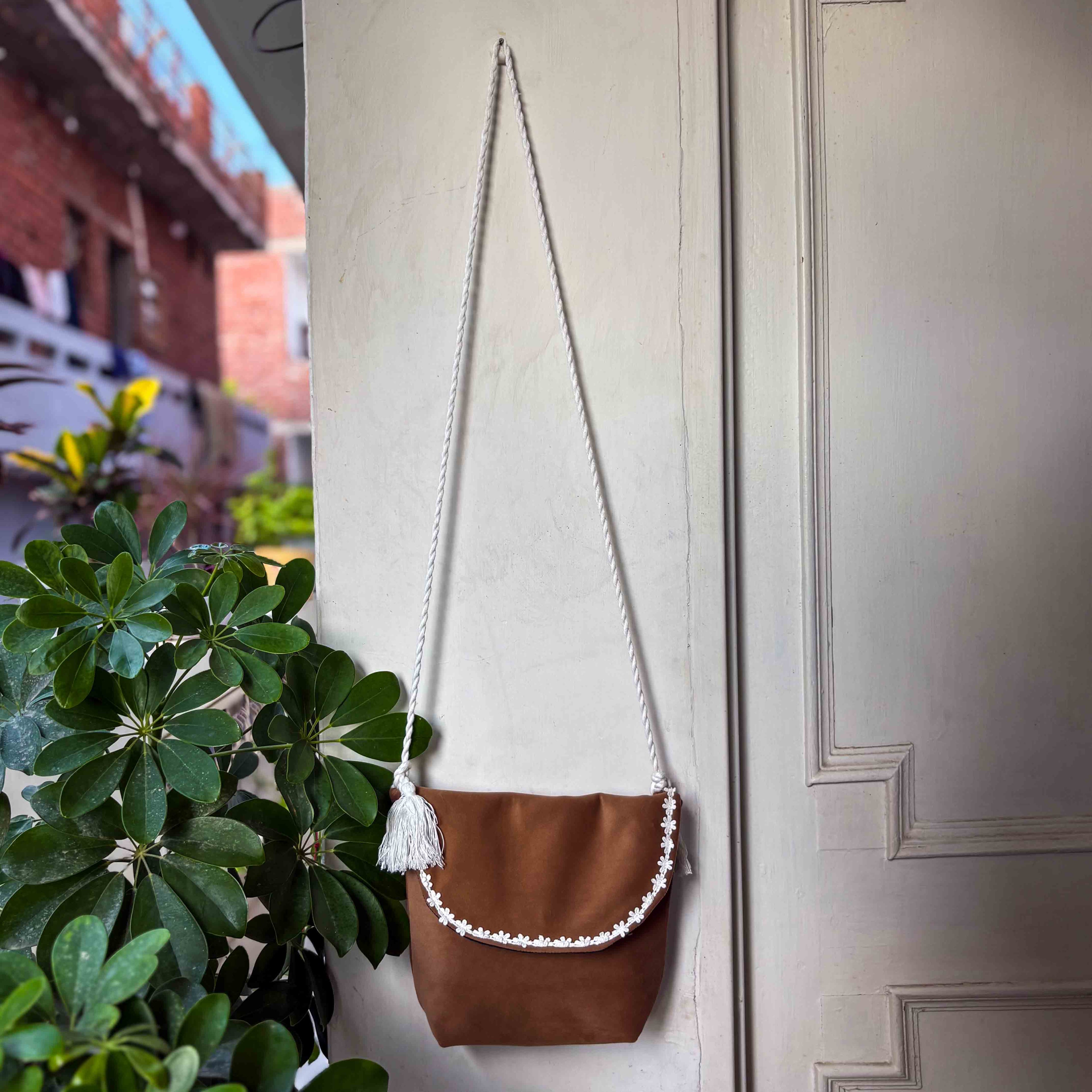 Brown leather handbag with white macramé strap hanging on a door