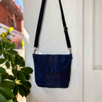Blue denim crossbody bag with denim strap against a white wall.