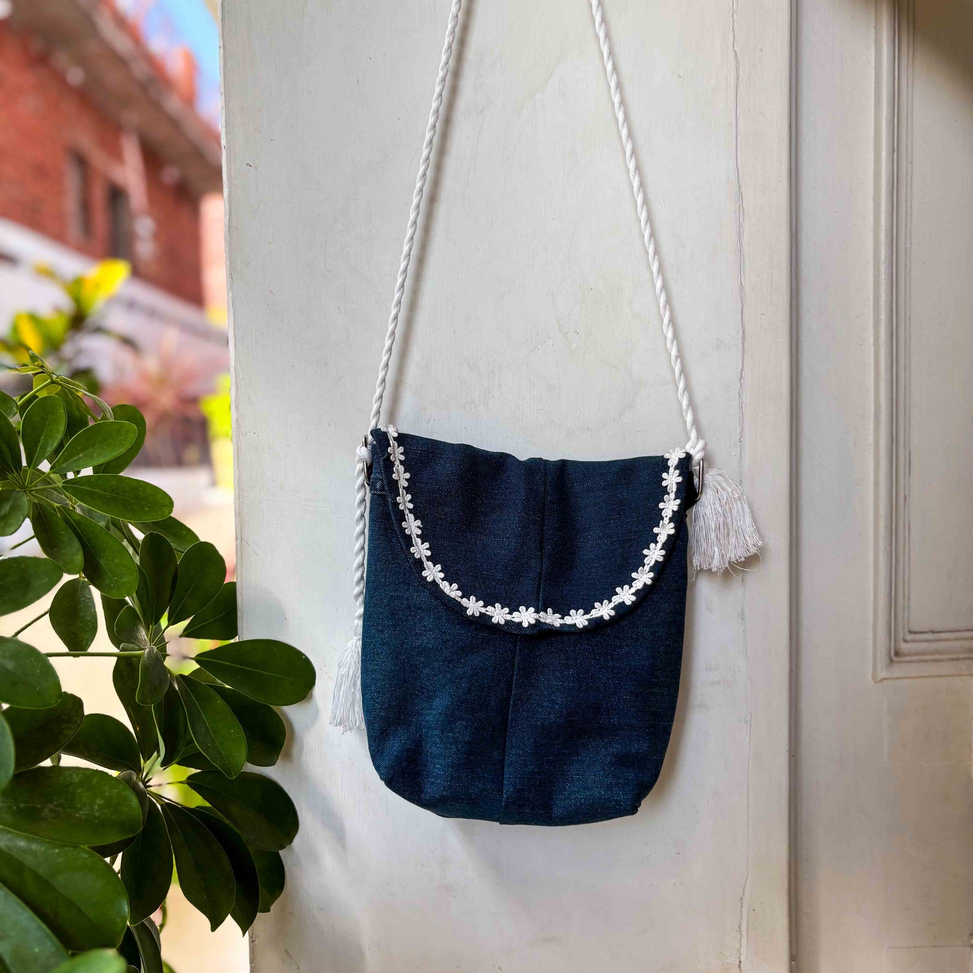Navy blue bag with white floral embroidery and tassels hanging on a white wall.