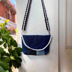 Blue denim handbag with white trim hanging on a white door