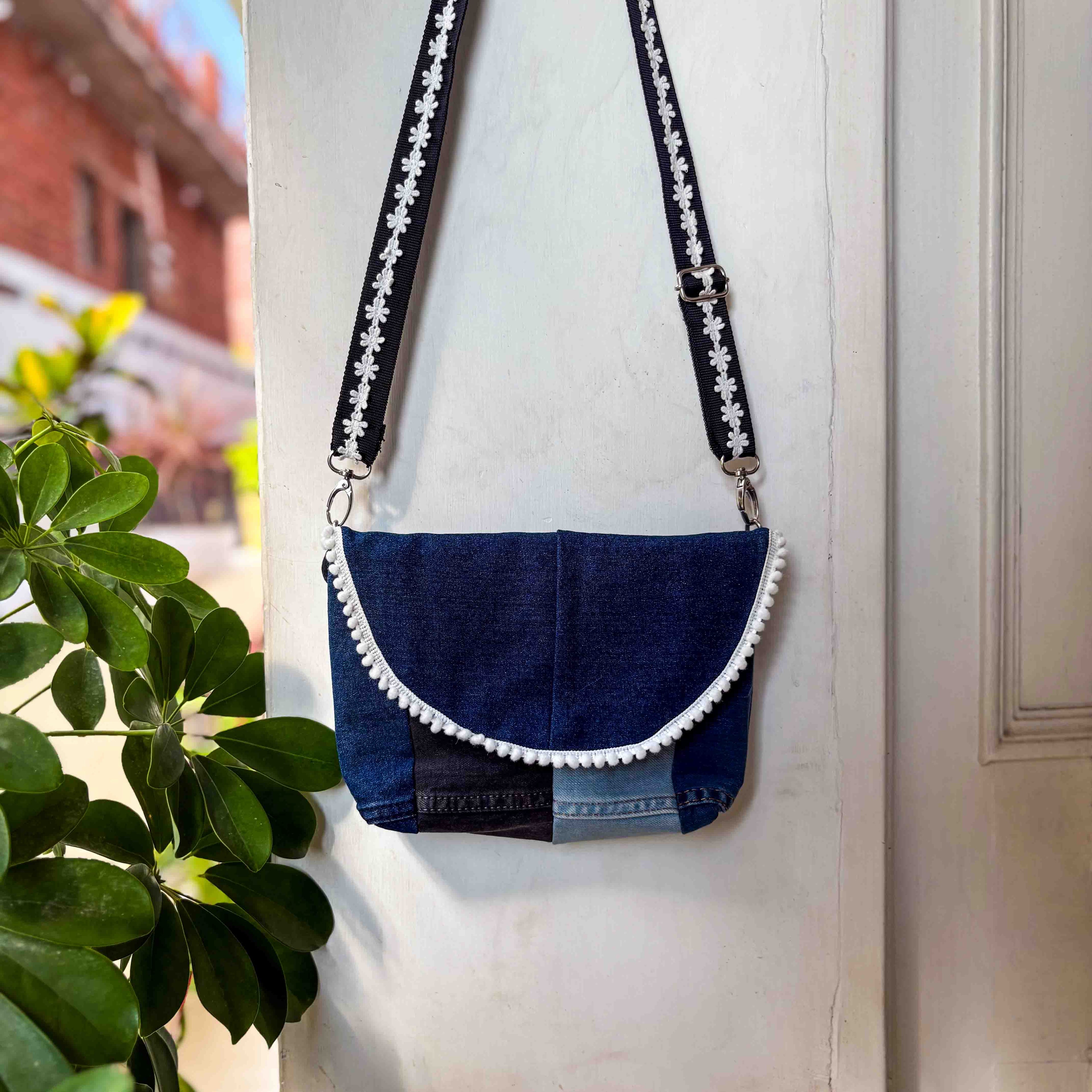 Blue denim handbag with white trim hanging on a white door