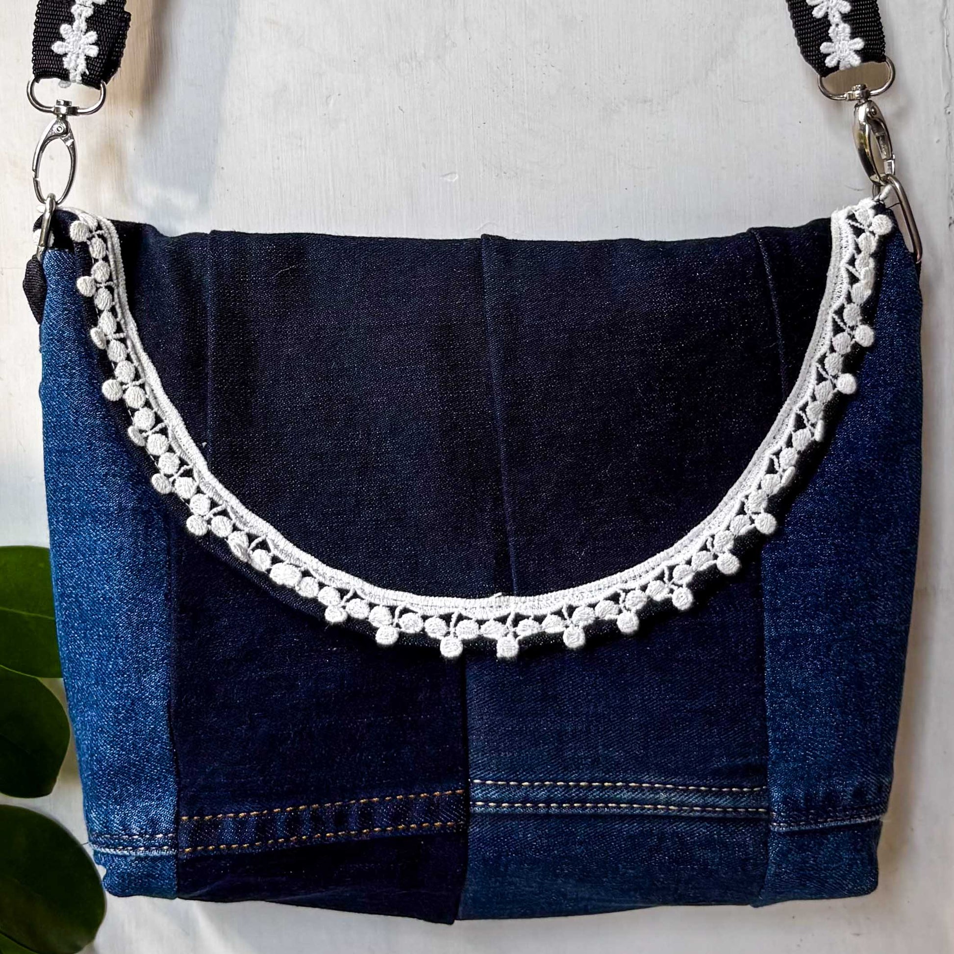 Blue denim handbag with decorative white trim on a white background