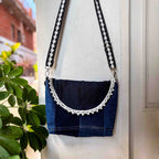 Blue denim bag with decorative strap against a neutral background