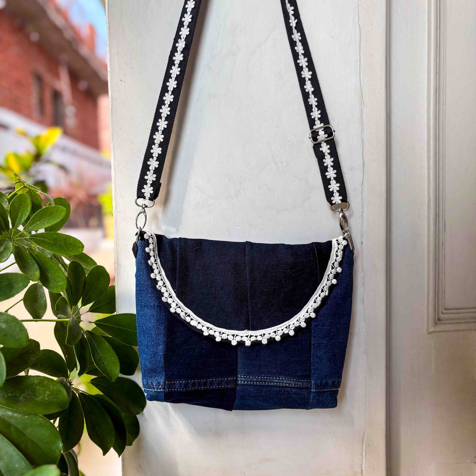 Blue denim bag with decorative strap against a neutral background