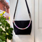 Black handbag with decorative chain strap against a white wall
