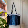 Blue and black tote bag with white trim hanging on a white door.
