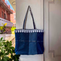 Blue denim tote bag with white embroidery hanging on a white door.