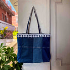 Blue denim tote bag with white embroidery hanging on a white door.