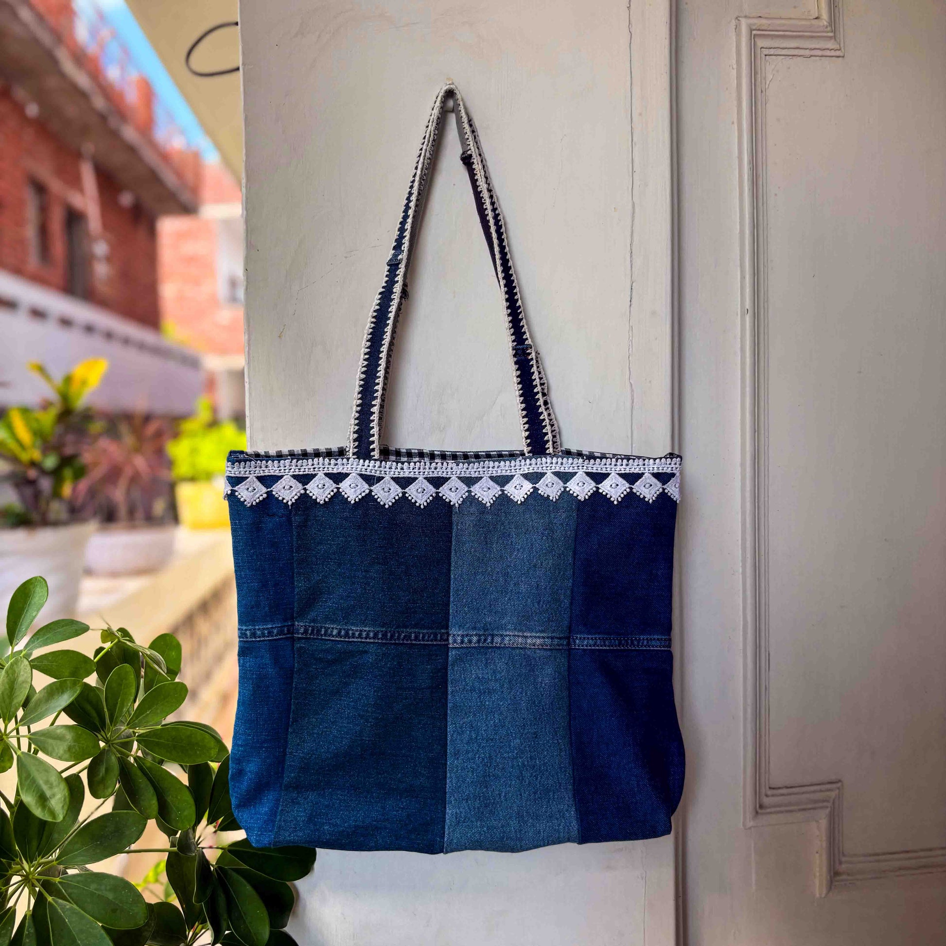 Blue denim tote bag with white embroidery hanging on a white door.