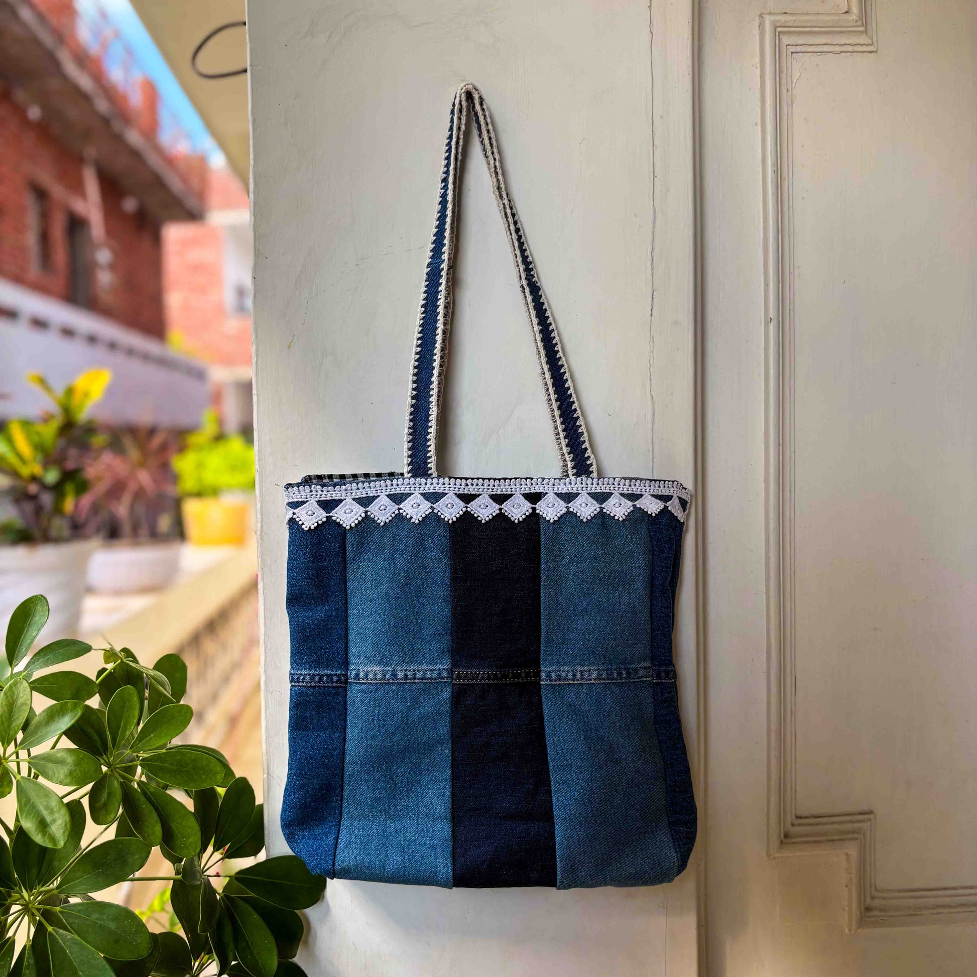 Blue striped tote bag with white lace trim hanging on a white door.