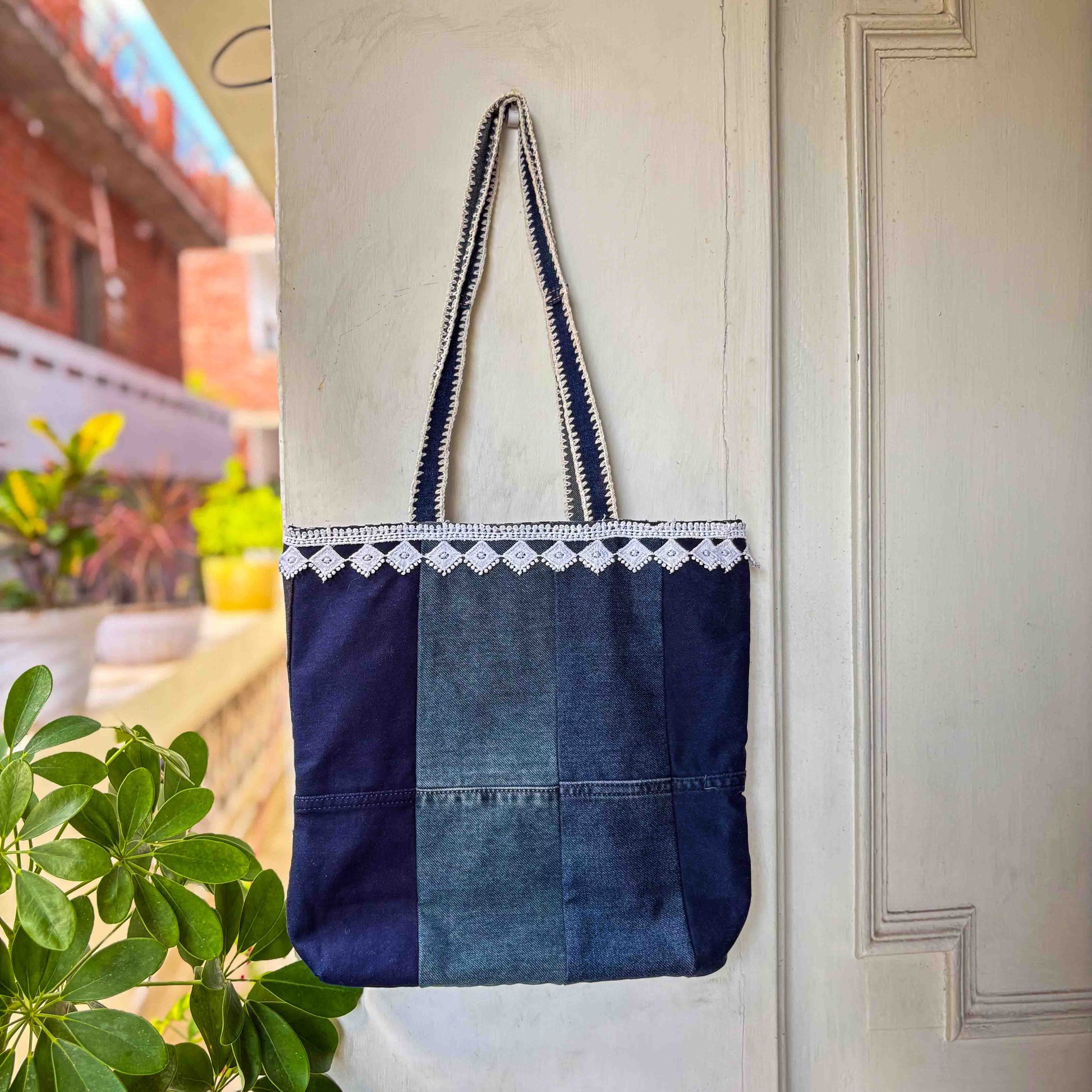 Blue denim tote bag with white lace trim hanging on a door.
