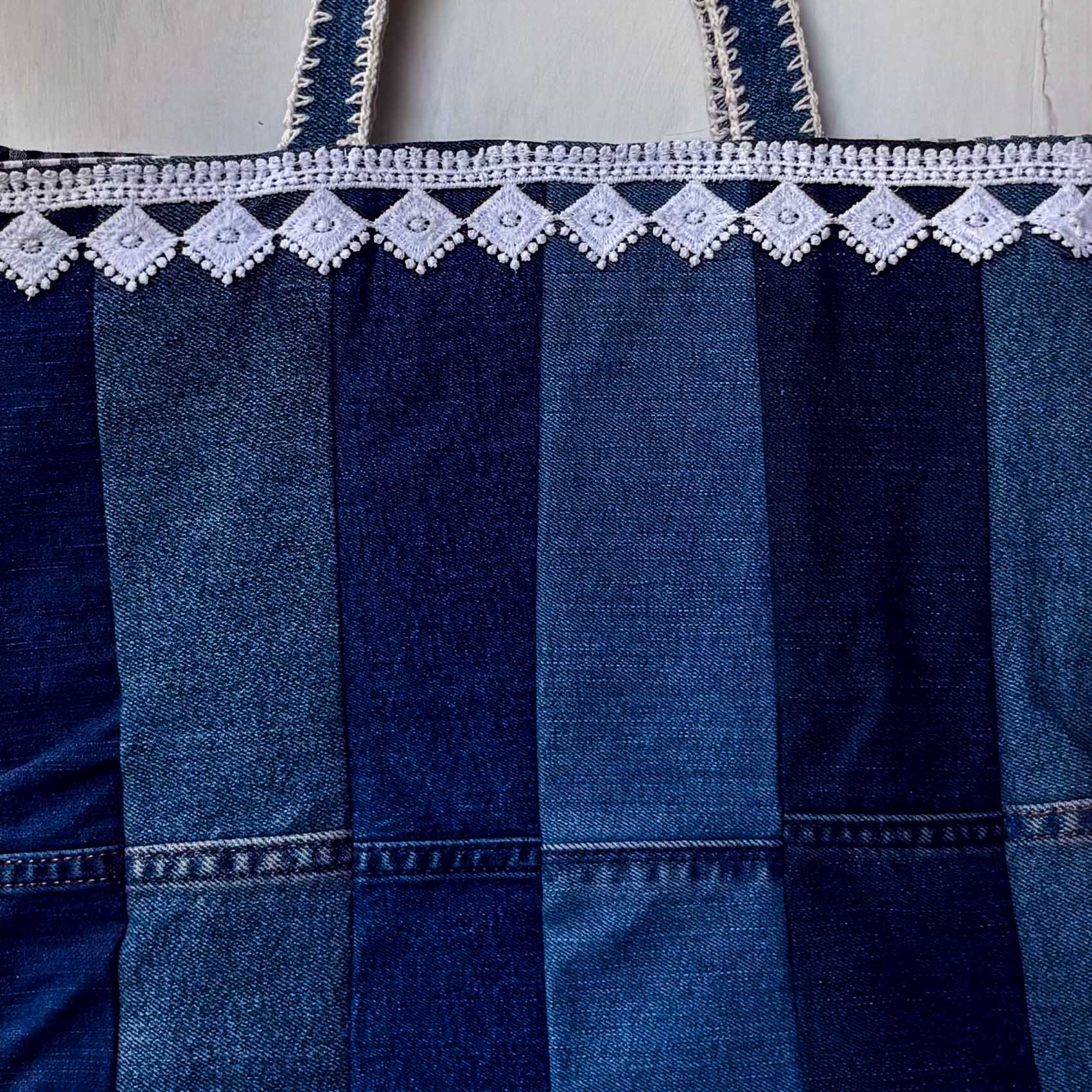 Blue denim bag with white lace detailing on a light wooden surface