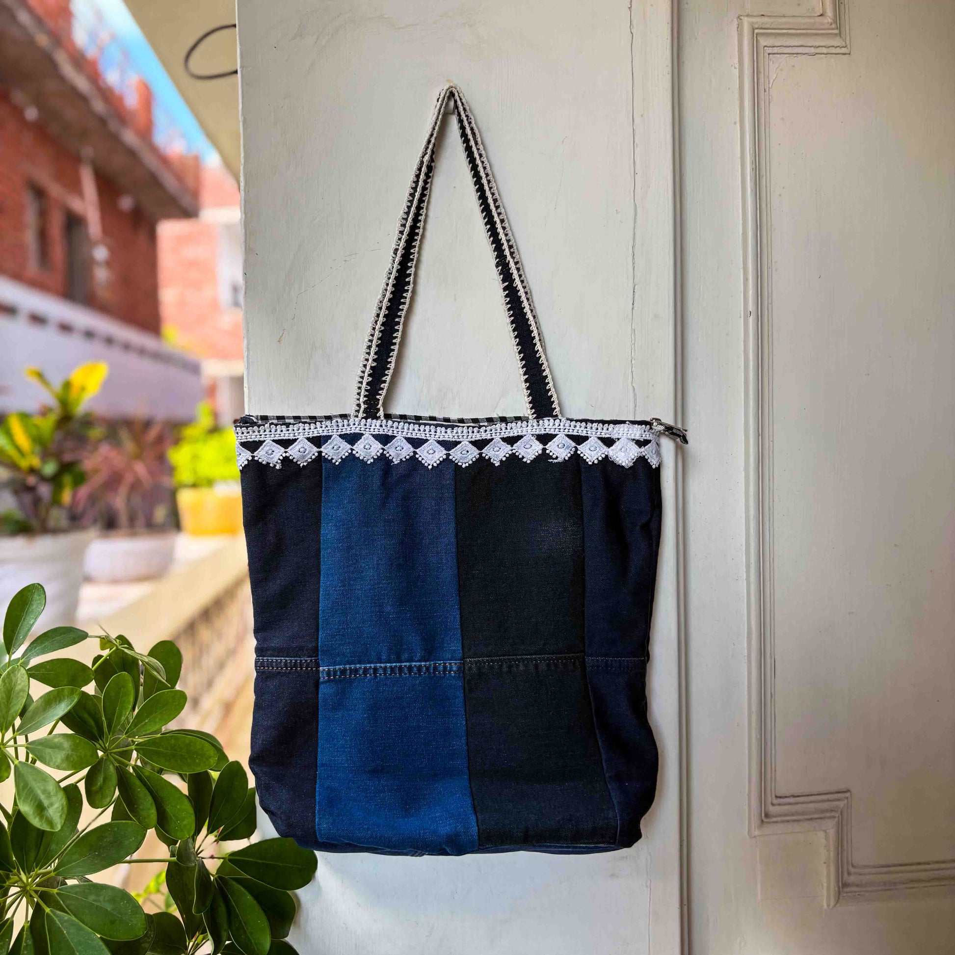 Blue and black tote bag with white lace trim hanging on a door.