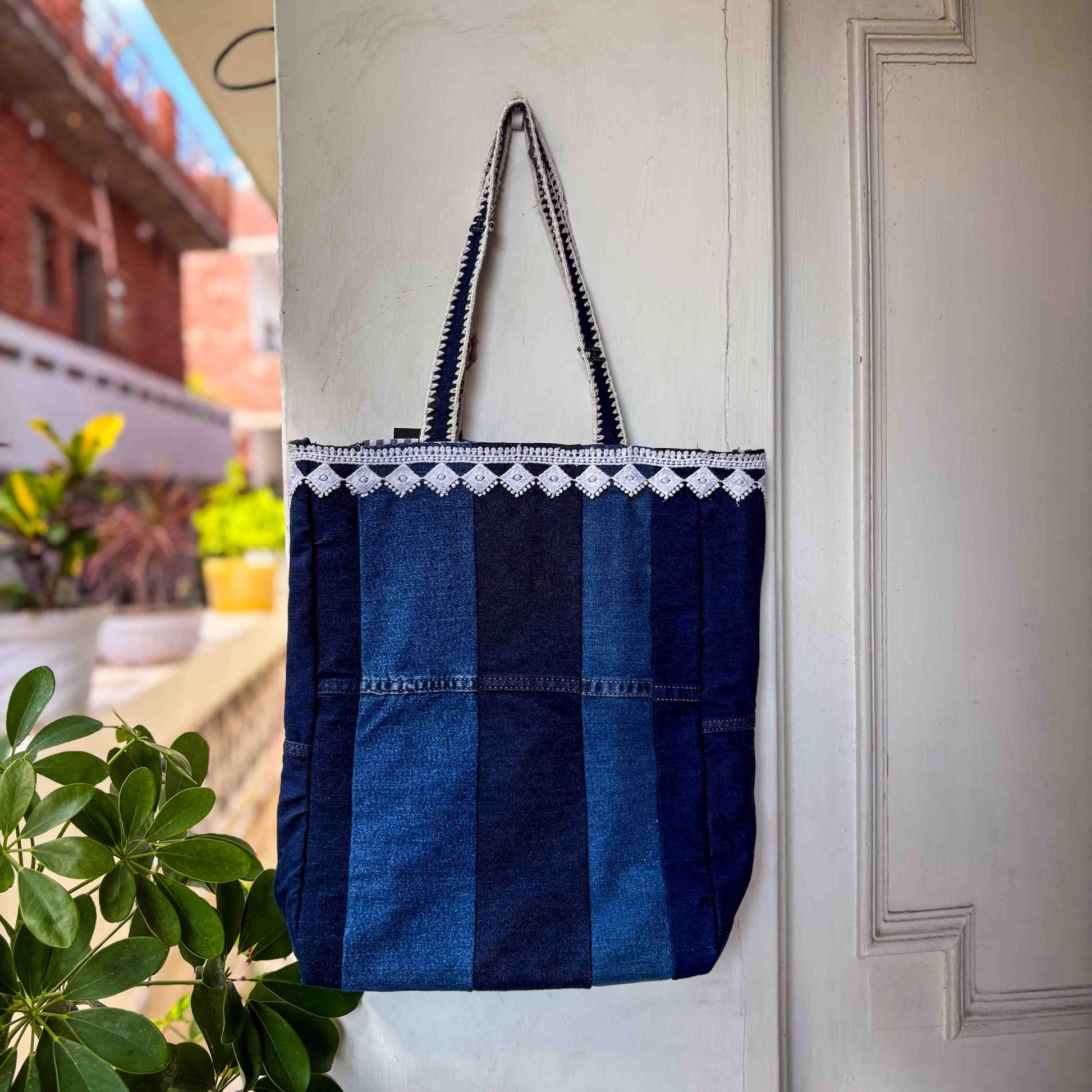 Blue striped tote bag with white lace trim hanging on a door.