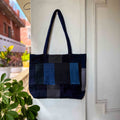 Patchwork tote bag with blue and black pattern hanging on a white door.