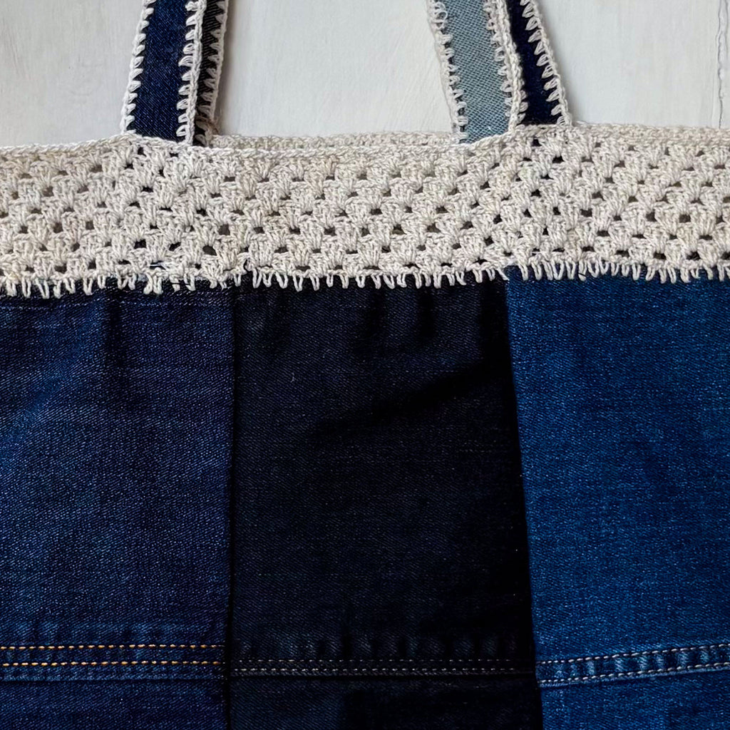 Blue denim bag with white crochet top section on a light gray background