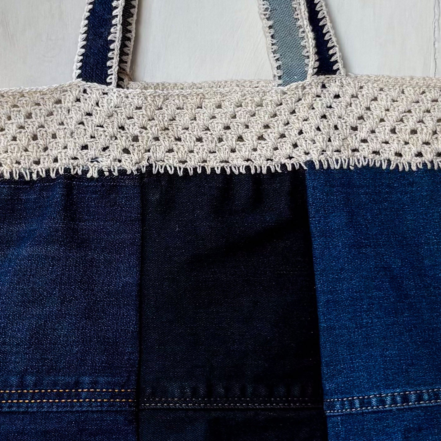 Blue denim bag with white crochet top section on a light gray background