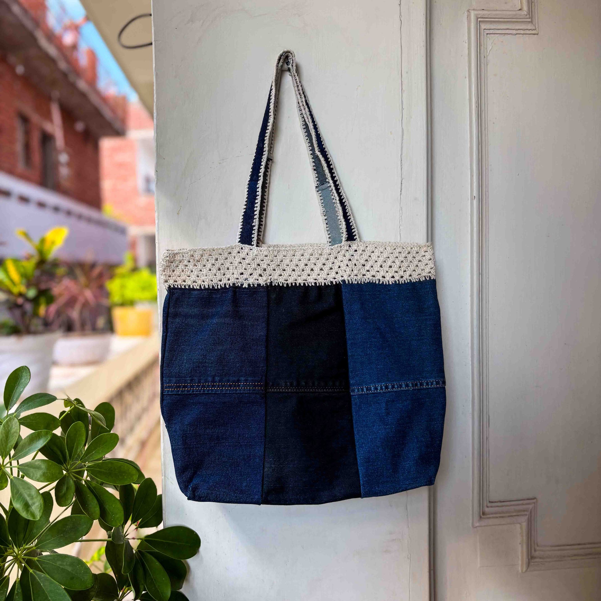 Blue tote bag with white crochet top section hanging on a white door.